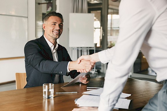 Zwei Geschäftspartner begrüßen sich mit Handschlag am Besprechungstisch